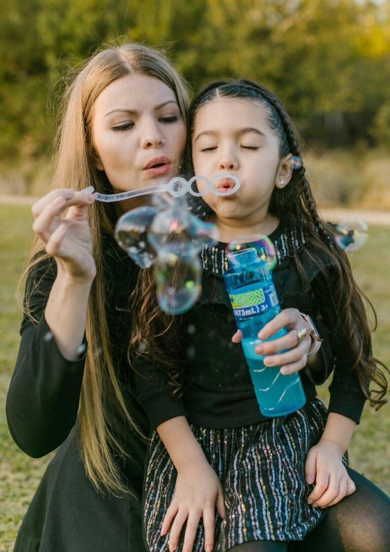A mother and daughter blowing bubbles on a sunny day, symbolizing joyful family moments and connection fostered by Rise, Roar, and Soar activities.