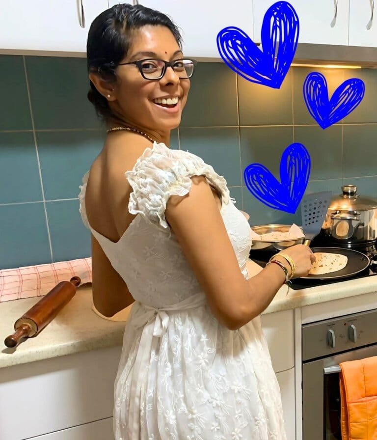 Varsha smiling while making roti in her kitchen, representing joy, mindfulness, and embracing life’s simple moments.